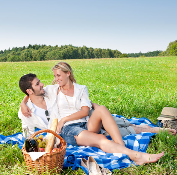 Young couple enjoying romantic picnic in green meadow by sunny day