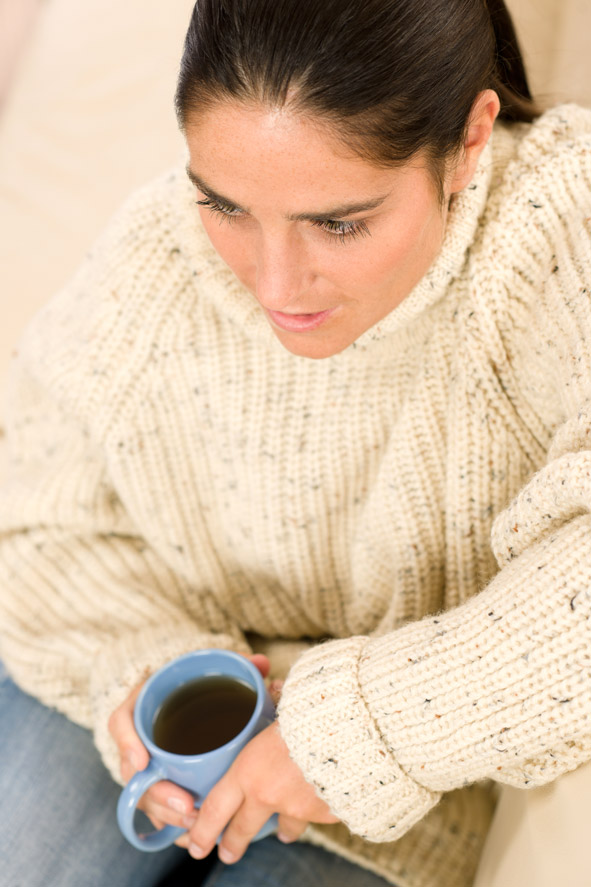 Young woman wearing winter wool sweater sitting home holding a blue tea mug
