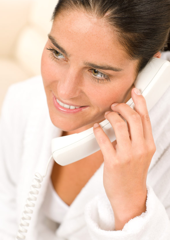Smiling young woman wearing a white bathrobe holding a white phone